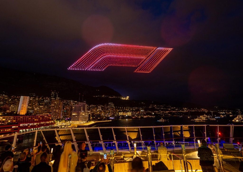 A red racing car formation made of drones above the illuminated Monaco harbour
